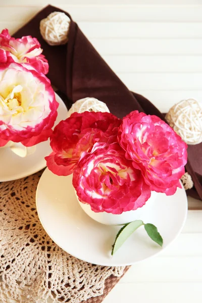 Roses in cups on napkins on wooden background — Stock Photo, Image