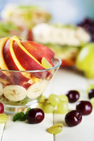 Salade de fruits savoureuse dans un bol en verre, sur une table en bois blanc — Photo