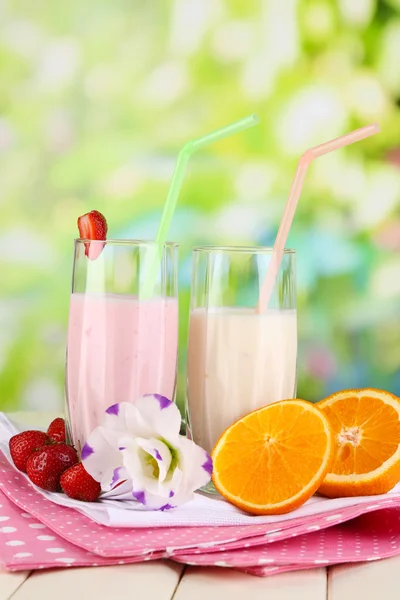 Délicieux milk shakes aux fraises et orange sur table en bois sur fond naturel — Photo