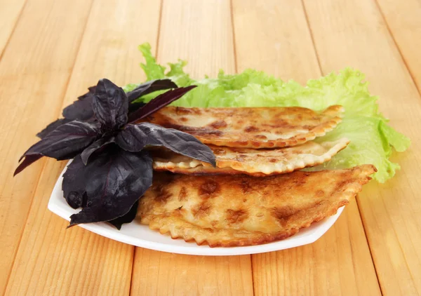 Gustosi chebureks con erbe fresche su piatto, su fondo di legno — Foto Stock