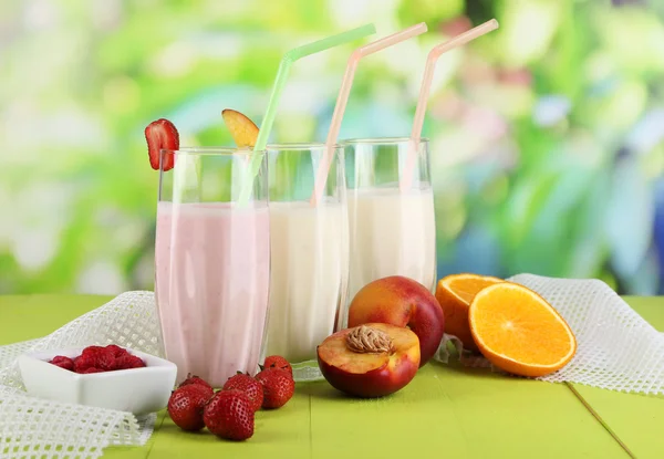 Leckere Milchshakes mit Erdbeeren und Pfirsich auf Holztisch vor natürlichem Hintergrund — Stockfoto
