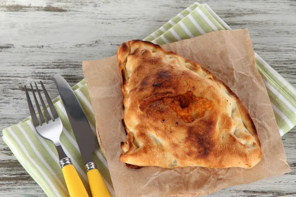 Pizza calzone su carta da lucido su tovagliolo su tavolo di legno — Foto Stock