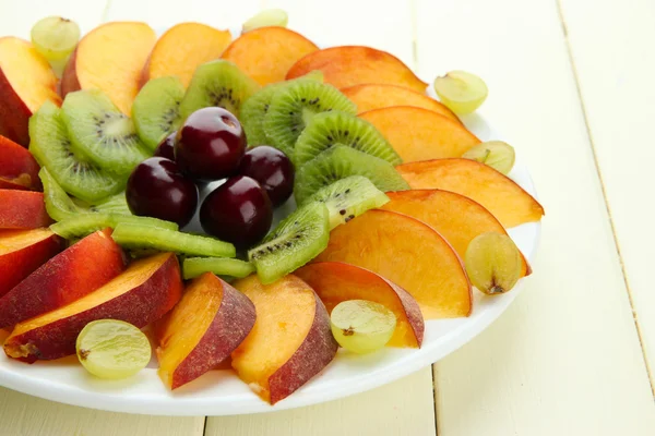 Assortment of sliced fruits on plate, on white wooden table — Stock Photo, Image