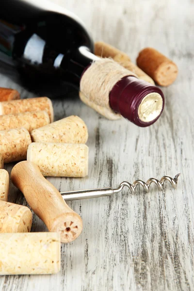 Corkscrew with wine corks and bottle of wine on wooden table close-up — Stock Photo, Image