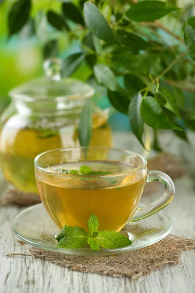 Чайник и чашка травяного чая со свежими мятными цветами на деревянном столе — стоковое фото
