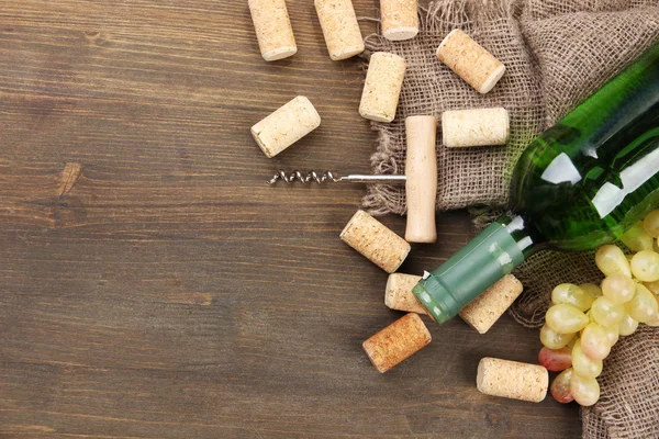 Fles wijn, druiven en kurken op houten achtergrond — Stockfoto