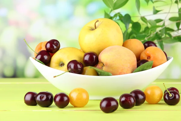 Bright summer fruits in plate on wooden table on natural background — Stock Photo, Image
