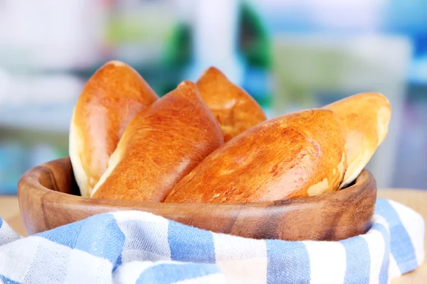 Fresh baked pasties, in wooden bowl, on wooden table, on bright background — Stock Photo, Image