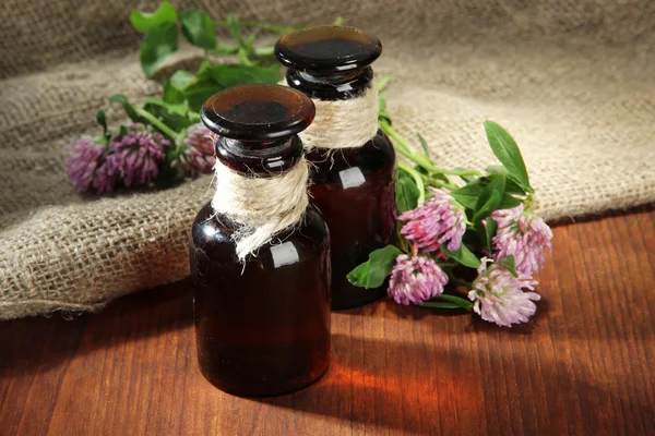 Medicin flaskor med klöver blommor på träbord med säckväv — Stockfoto