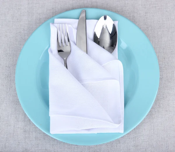 Folded napkin with fork, spoon and knife, on plate, on color background — Stock Photo, Image