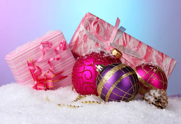 Vackra julgranskulor och gåvor på snö på ljus bakgrund — Stockfoto