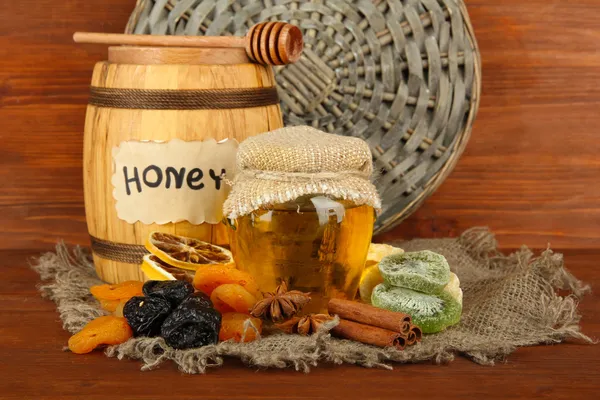 Jar of honey, wooden barrel, drizzler and dried fruits on wooden background — Stock Photo, Image