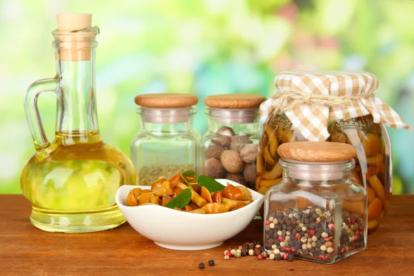 Composición de deliciosos champiñones marinados, aceite y especias sobre mesa de madera sobre fondo brillante —  Fotos de Stock