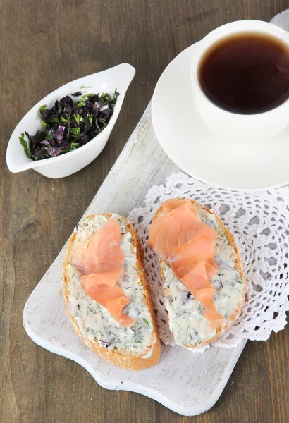 Fisk smörgåsar och kopp te på skärbräda på träbord — Stockfoto