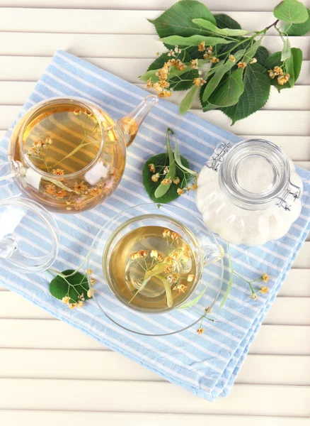 Hervidor de agua y taza de té con tilo en servilleta sobre mesa de madera —  Fotos de Stock