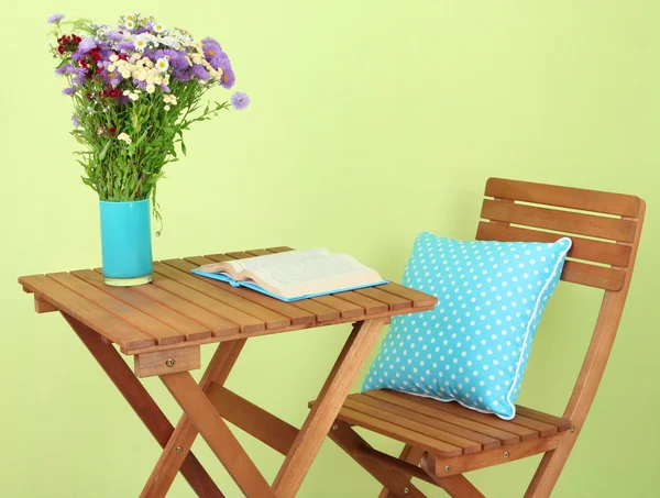 Деревянный стол с цветами и книга на зеленом фоне — стоковое фото