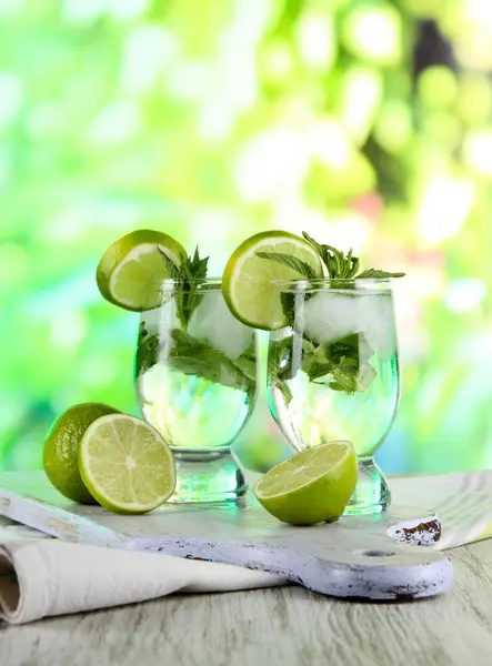 Vasos de cóctel con hielo a bordo en servilleta sobre mesa de madera sobre fondo natural — Foto de Stock