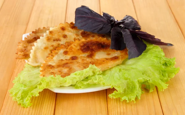 Sabrosos chebureks con hierbas frescas en el plato, sobre fondo de madera — Foto de Stock