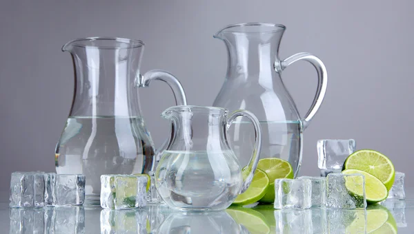 Glas kannor vatten med is och lime på grå bakgrund — Stockfoto