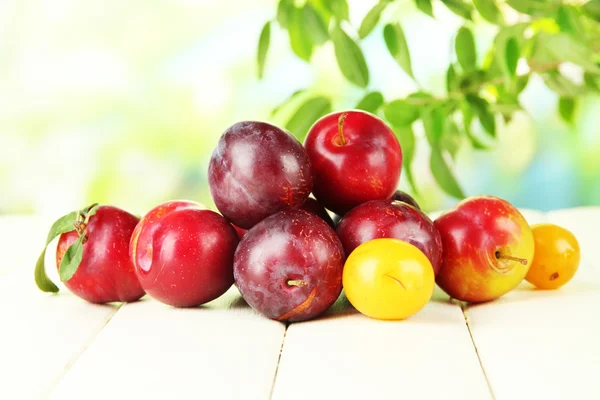 Ripe plums on wooden table on natural background — Stock Photo, Image