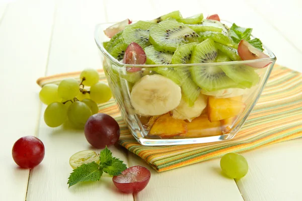 Tasty fruit salad in glass bowl, on white wooden table — Stock Photo, Image