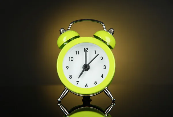 Green alarm clock on dark yellow background — Stock Photo, Image