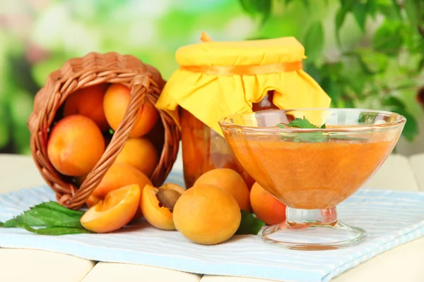 Apricot jam in glass jar and fresh apricots, on wooden table, on bright background — Stock Photo, Image