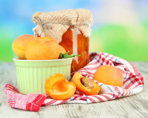 Confiture d'abricots dans un bocal en verre et abricots frais, sur table en bois, sur fond lumineux — Photo