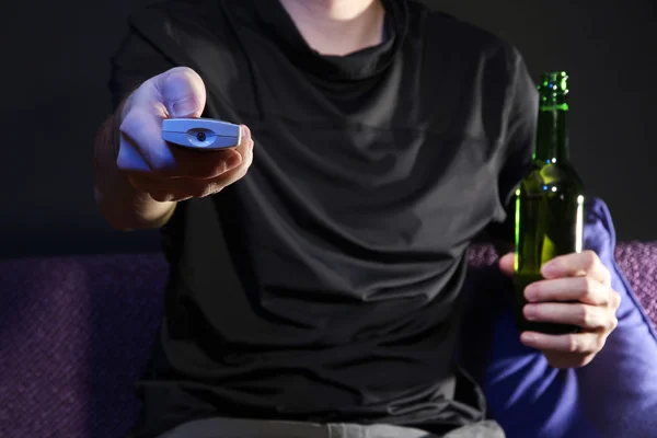 Man hand een tv met afstandsbediening en bierfles, op donkere achtergrond — Stockfoto