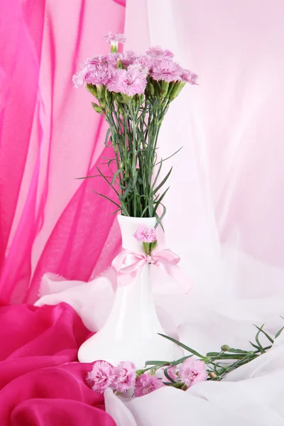 Veel kleine roze teentjes in vaas op lichte stof achtergrond — Stockfoto