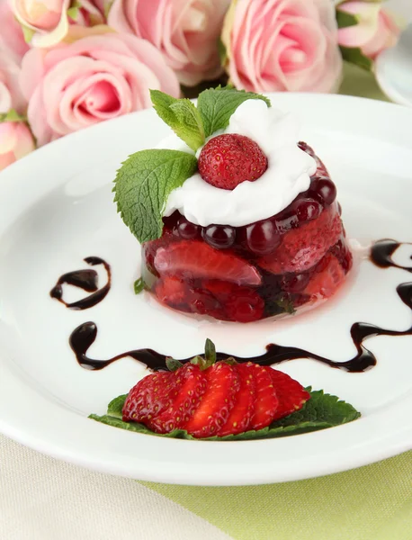 Вкусный желейный десерт со свежими ягодами, на фоне розовых роз — стоковое фото