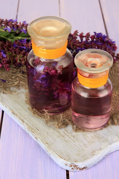 Medicine bottles with salvia flowers on purple wooden background — Stock Photo, Image