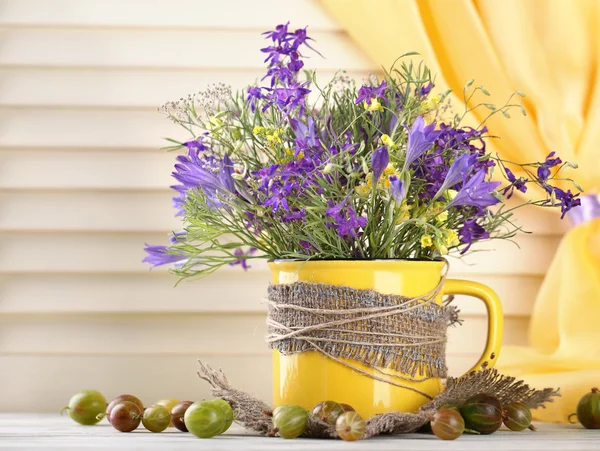 Hermoso ramo de flores silvestres en taza y bayas en mesa de madera —  Fotos de Stock