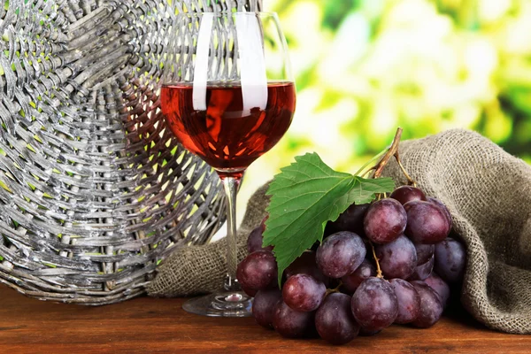 Ripe delicious grapes with glass of wine on table on bright background — Stock Photo, Image