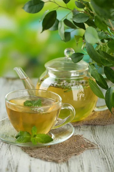 Tetera y taza de té de hierbas con flores de menta fresca en la mesa de madera —  Fotos de Stock