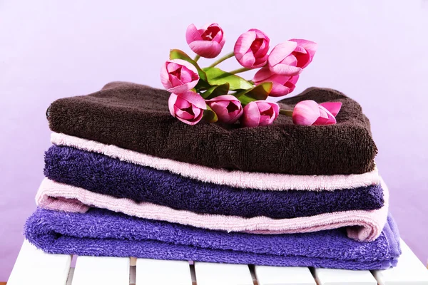 Towels and flowers on wooden chair on purple background