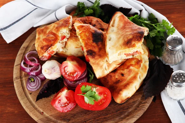 Pizza calzones on wooden board near napkin on wooden table — Stock Photo, Image