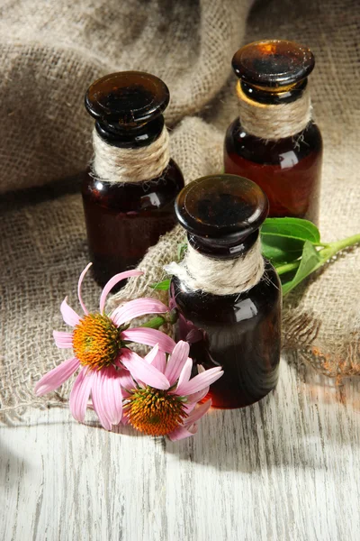 Bottiglie medicinali con fiori di echinacea viola su tavolo di legno con iuta — Foto Stock