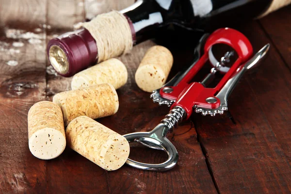 Corkscrew with wine corks and bottle of wine on wooden table close-up — Stock Photo, Image