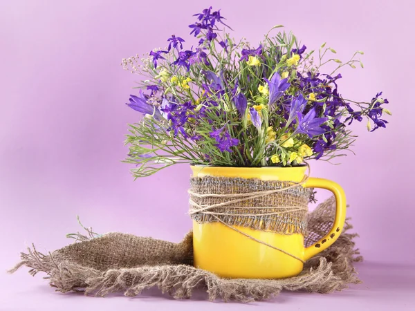 Mooi boeket van wilde bloemen in cup op paarse achtergrond — Stockfoto