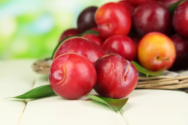 Ripe plums in basket on wooden table on natural background — Stock Photo, Image