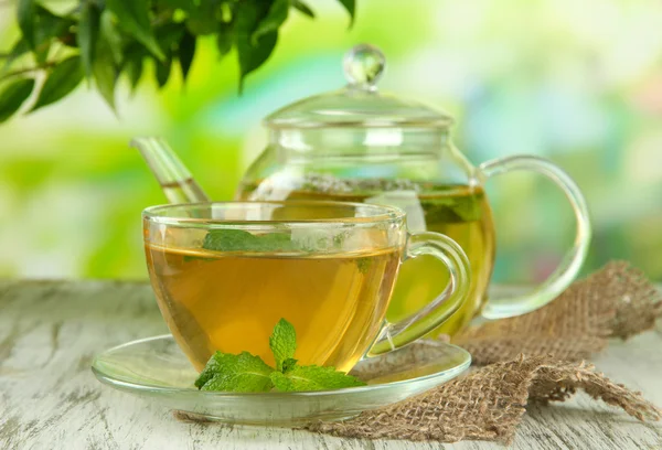 Teekanne und Tasse Kräutertee mit frischen Minzblüten auf Holztisch — Stockfoto