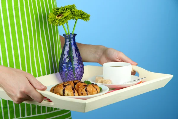 Woman in green apron holding wooden tray with breakfast, on color background — Stock Photo, Image