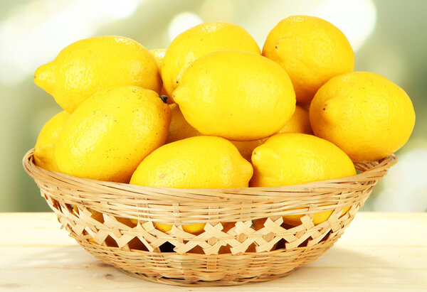 Ripe lemons in wicker basket on table on bright background