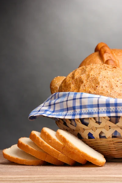 Delizioso pane in cesto su tavolo di legno su sfondo grigio — Foto Stock