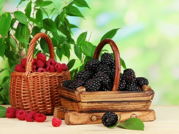 Ripe raspberries and blackberries in basket on wooden table on natural background — Stock Photo, Image