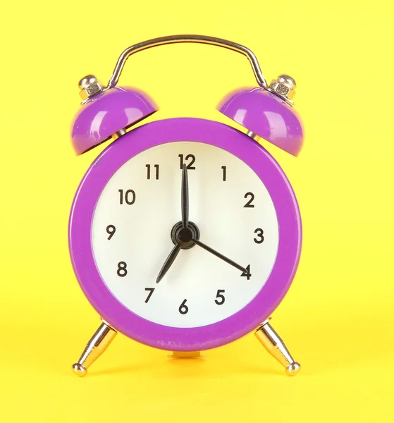 Reloj despertador púrpura sobre fondo amarillo — Foto de Stock