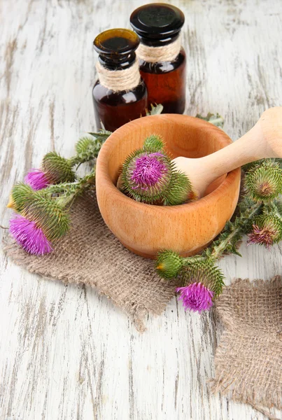 Botellas de medicina y mortero con flores de cardo sobre fondo de madera —  Fotos de Stock