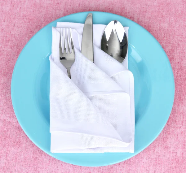 Folded napkin with fork, spoon and knife, on plate, on color background — Stock Photo, Image