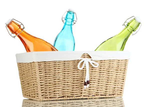 Botellas de vidrio de color en canasta de mimbre, aisladas en blanco — Foto de Stock